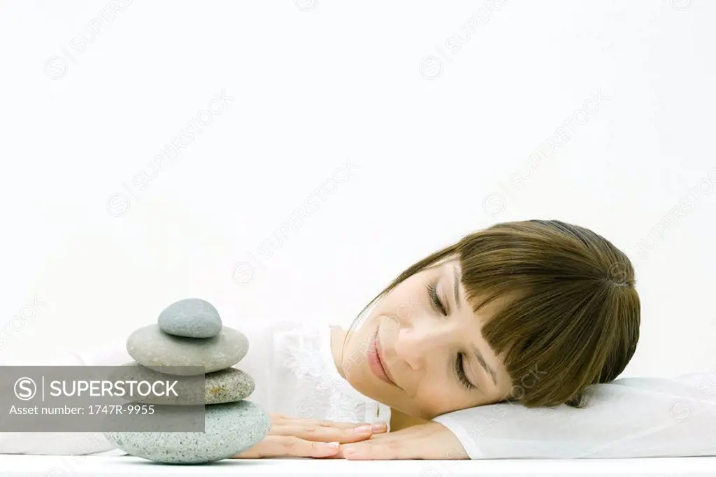 Woman resting head on arms, looking at stacked pebbles, smiling