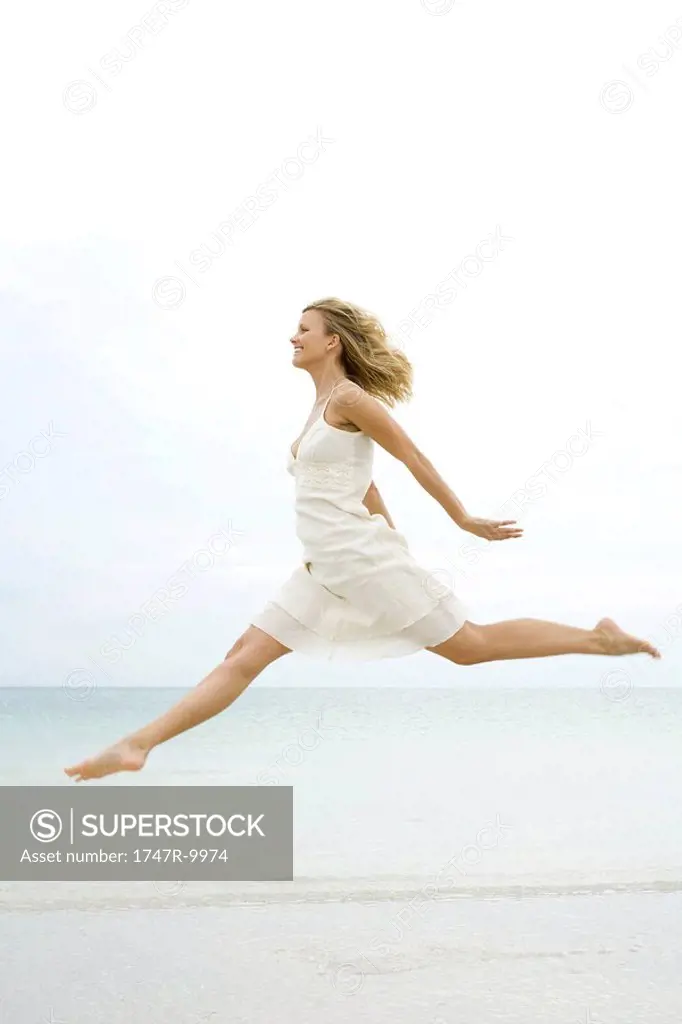 Woman jumping in the air at the beach, side view