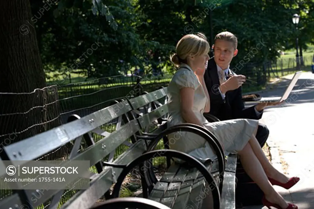 Businessman and businesswoman sitting on a park bench