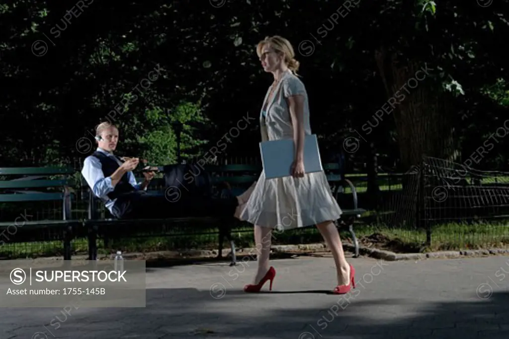 Businesswoman walking with a businessman reclining on a park bench