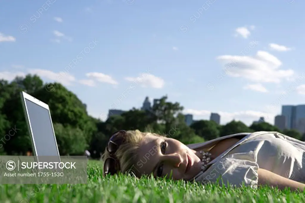 Young woman lying in a park with a laptop under her head