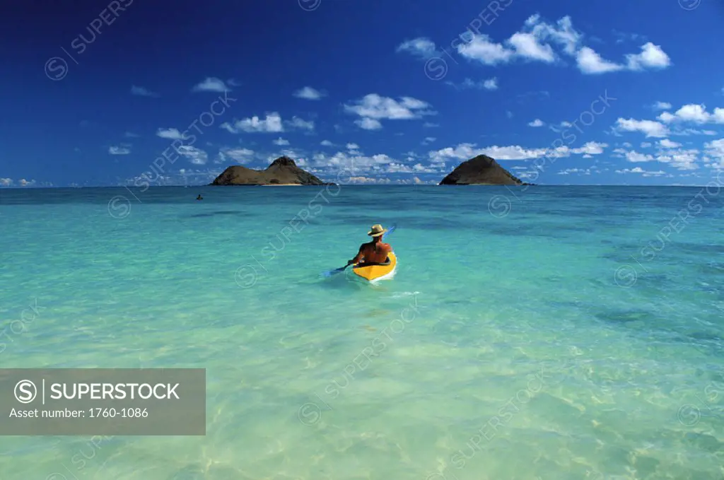 Hawaii, Oahu, Back view of man wearing hat on kayak heading to Mokulua Islands, blue skies