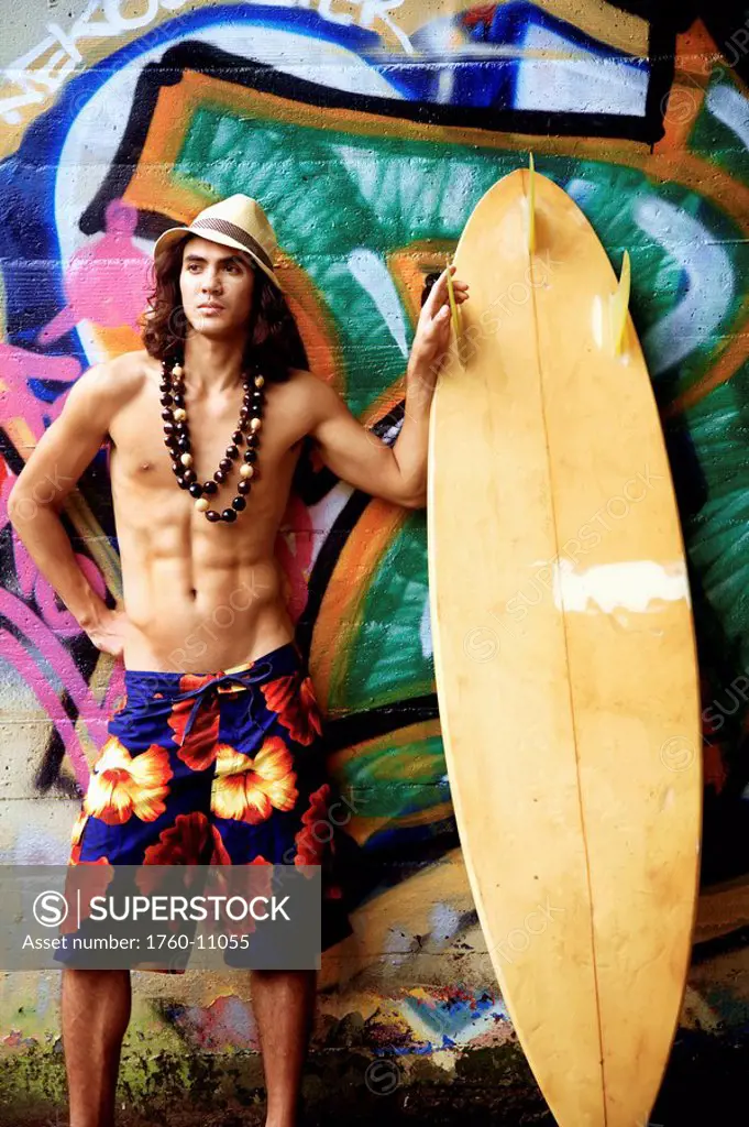Hawaii, Oahu, Young male posing infront of a graphic wall with surfboard.