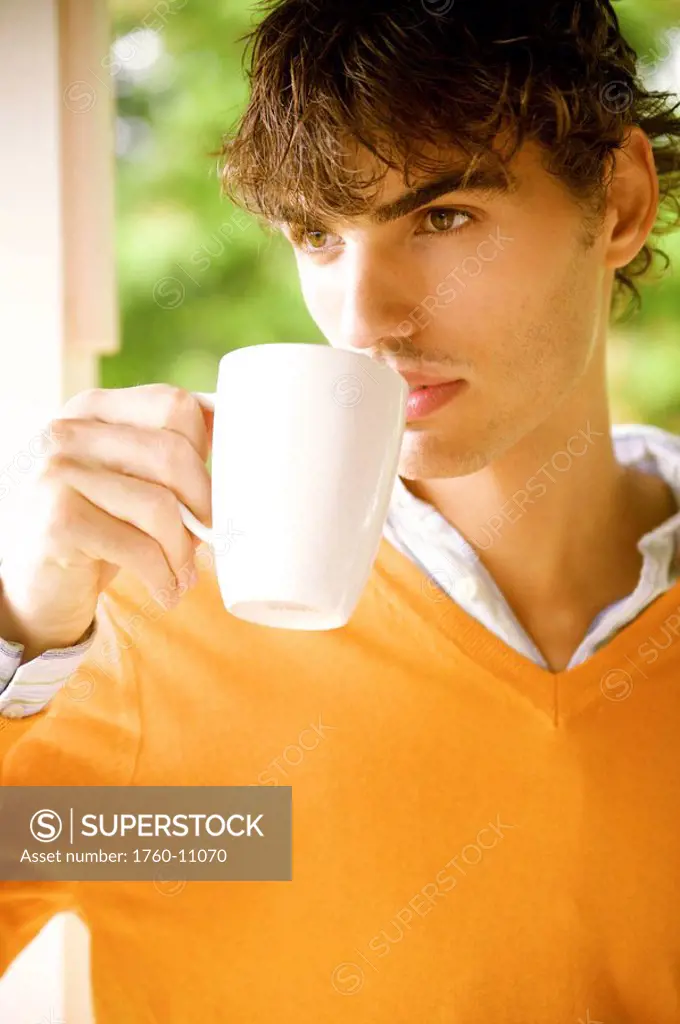 Hawaii, Portrait of a European Male Model in orange sweater drinking coffee.