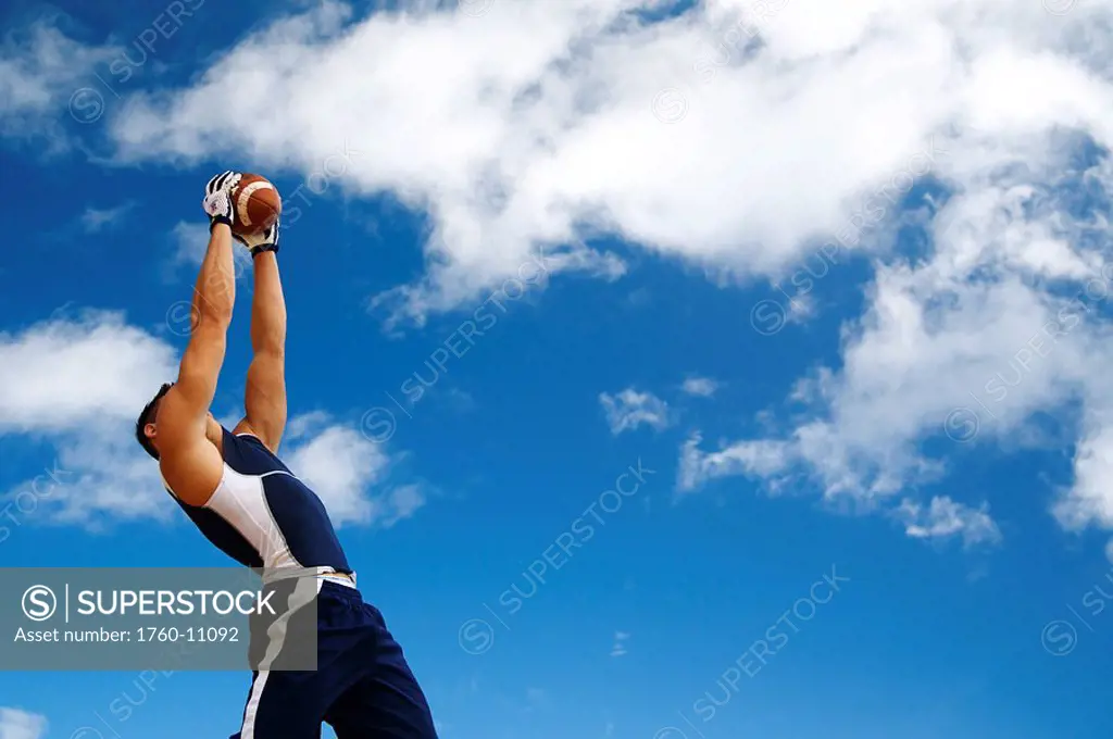 Hawaii, Kauai, Haena beach, Fit male holding a football with beautiful clouds in the background.