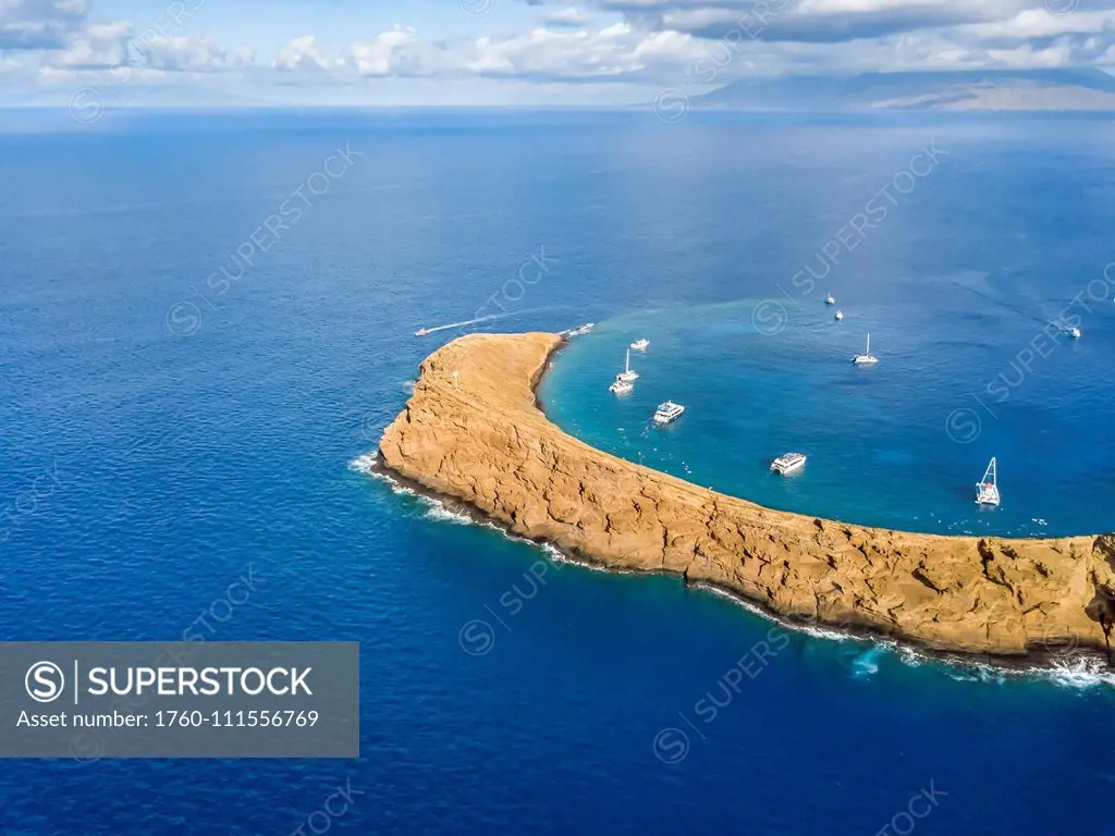 Molokini Crater, aerial shot looking at the backwall of the crescent shaped islet at mid-morning with charter boats inside; Maui, Hawaii, United State...