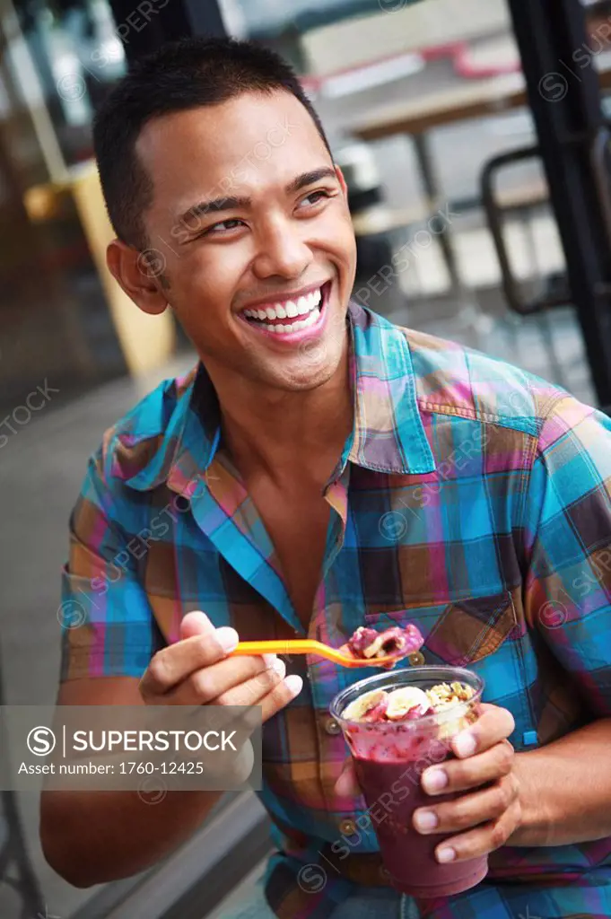 Hawaii, Oahu, Young local man eating and enjoying a delicious Acai cup.