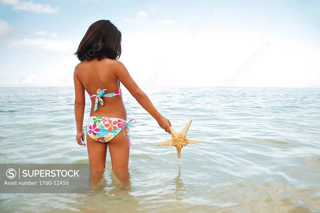 Hawaii, Oahu, Young girl holding a starfish, view from behind.