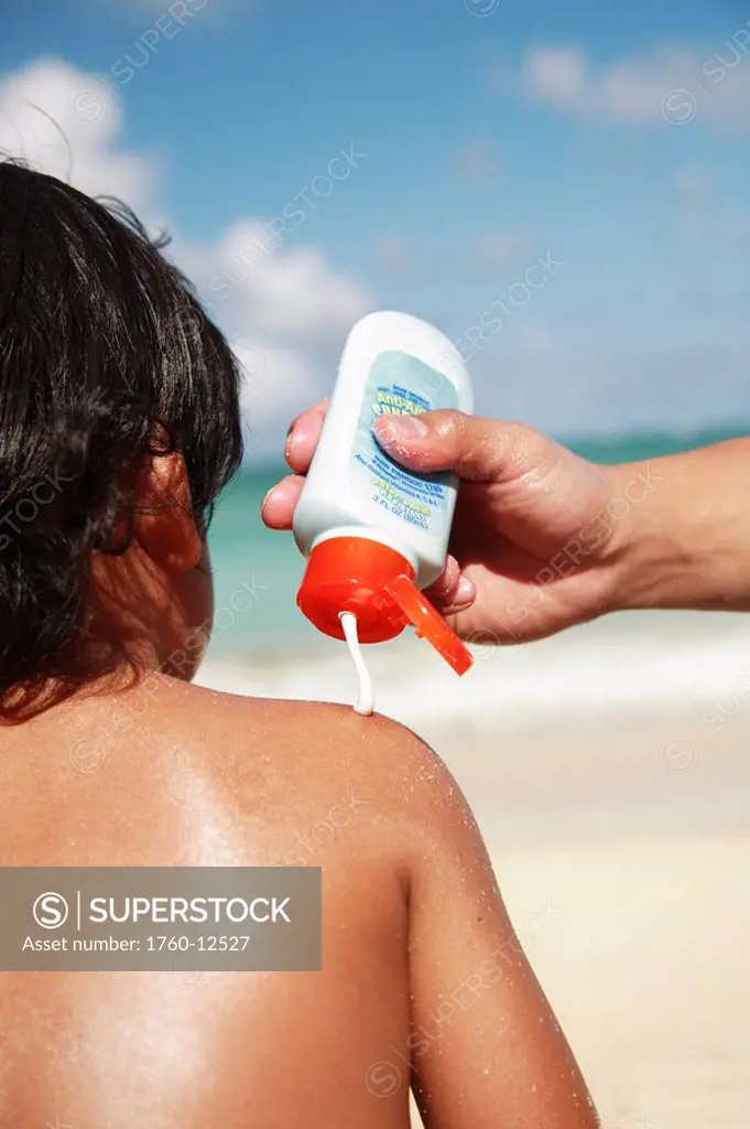 Hawaii, Oahu, Parent putting Sunscreen lotion on child´s shoulder at the beach
