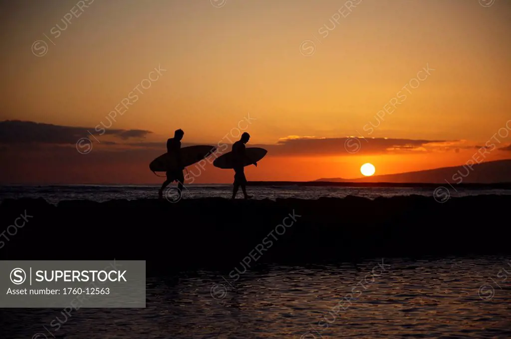 Hawaii, Oahu, Waikiki, Two Surfers walking along the shoreline as the beautiful sunsets