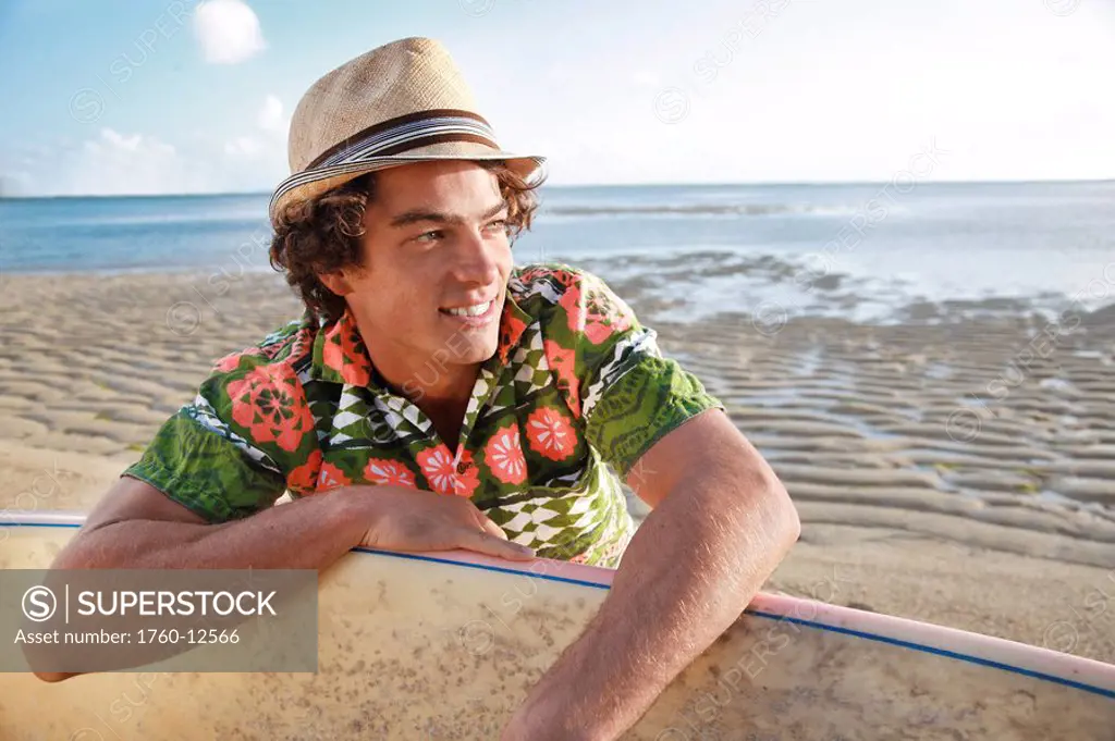 Hawaii, Oahu, Male relaxing on the beach with his surfboard wearing retro hawaiian shirt.