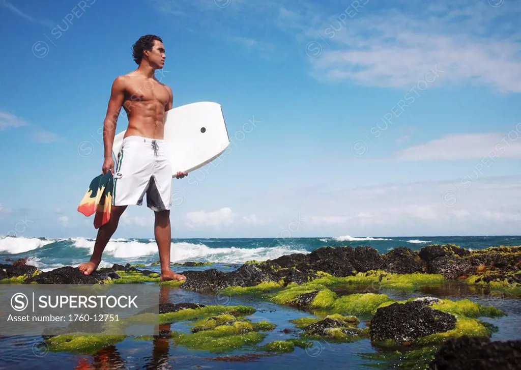 Hawaii, Oahu, Local bodyboarder standing on tidepool of rocks near the shoreline.