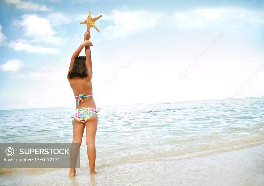 Hawaii, Oahu, Young girl holding a starfish, view from behind.