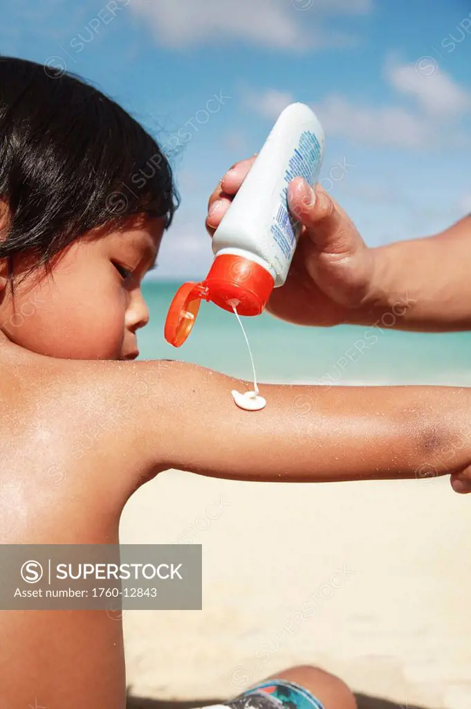Hawaii, Oahu, Parent putting Sunscreen lotion on child´s arm at the beach