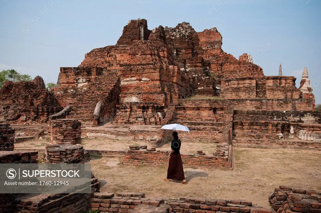 Thailand, Ayutthaya, Woman visitor with umbrella at Wat Mahathat Buddhist temple ruins.