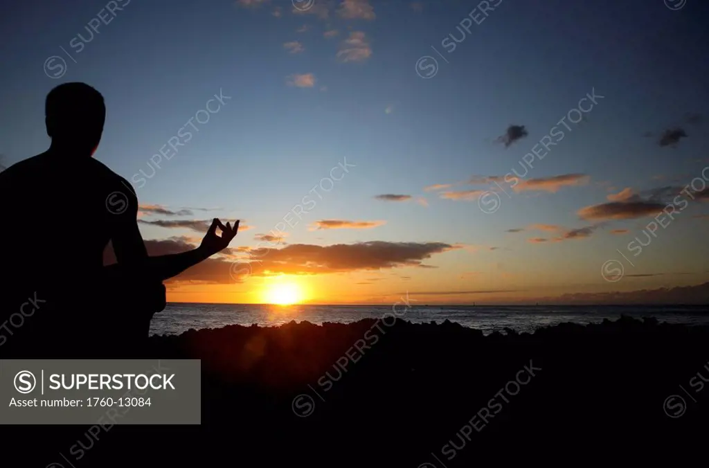 Hawaii, Oahu, Silhouette of a man meditating yoga as the sunsets