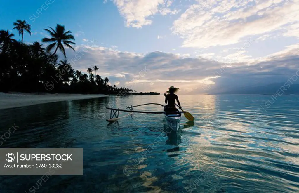 French Polynesia, Moorea, Woman paddling in outrigger canoe along shoreline.