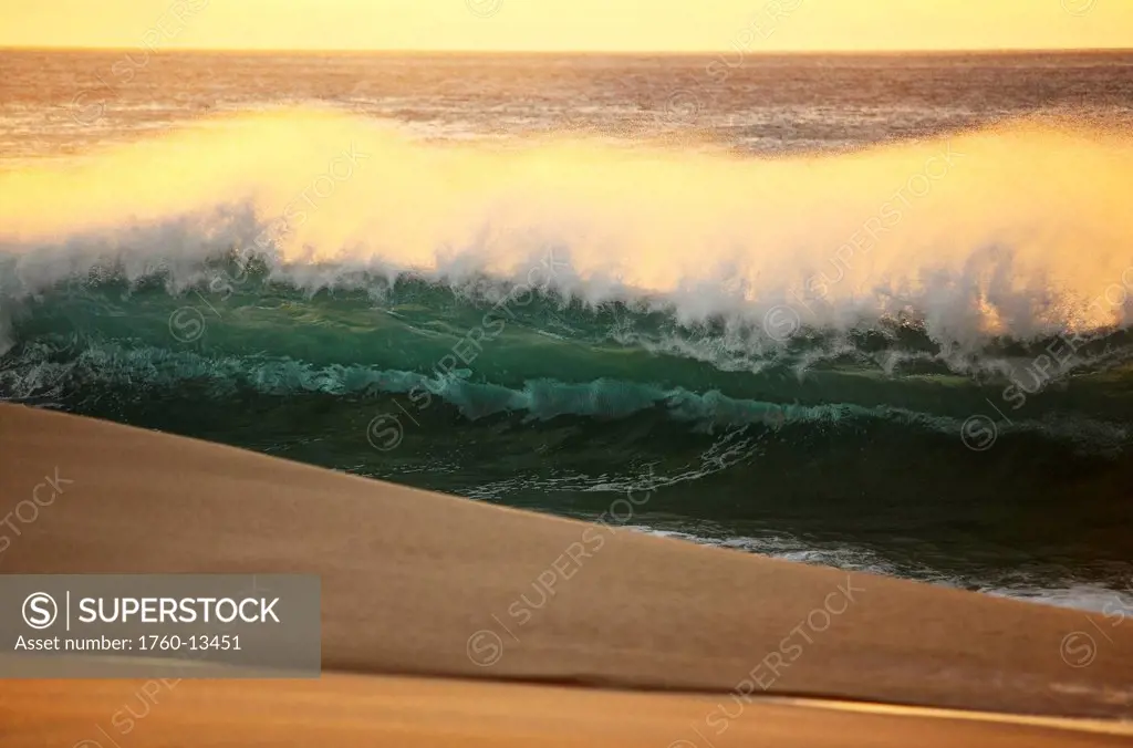 Hawaii, Oahu, North Shore, Sunset light illuminating ocean wave along beach.
