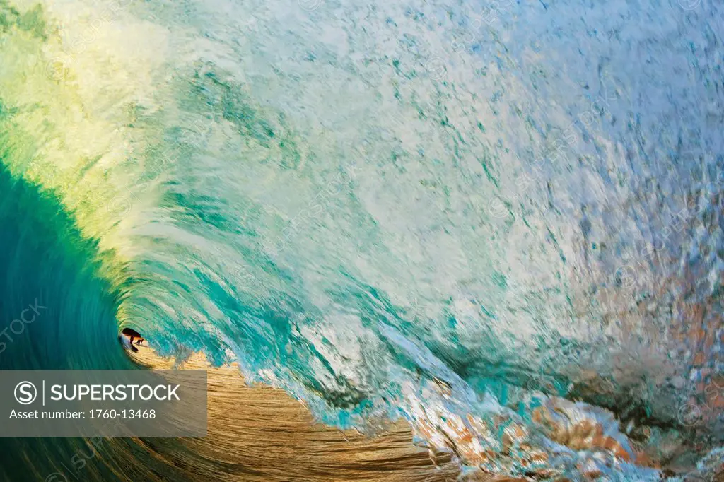 Hawaii, Maui, Makena Beach, View of distant surfers through barrel of turquoise wave, Sunset light.