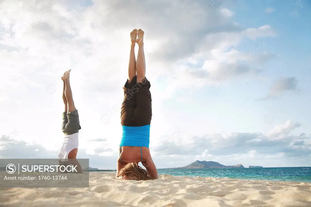 Hawaii, Oahu, Lanikai, Young couple doing yoga, stay in a headstand position on the beach.