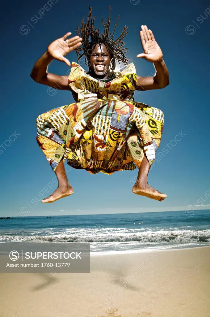 Hawaii, Kauai, Kealia Beach, African Dancer leaping in the air on sandy shore.