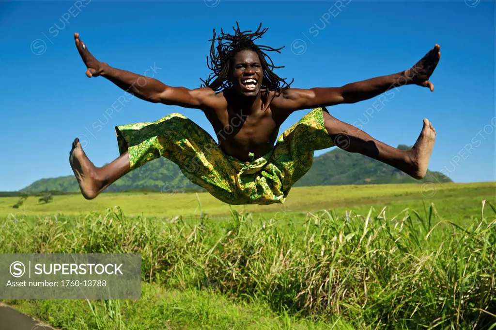 Hawaii, Kauai, Kealia, African dancer leaping into the air along grassy roadside.