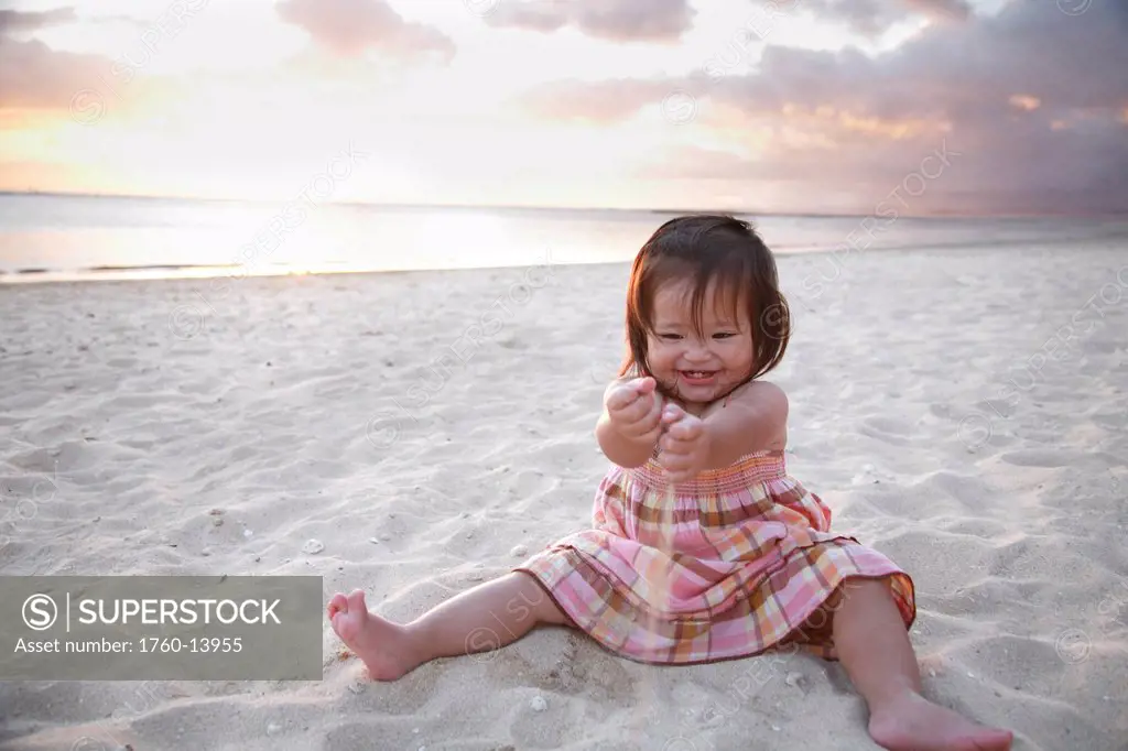 Hawaii, Oahu, Young toddler girl plays in sand at beach during sunset.