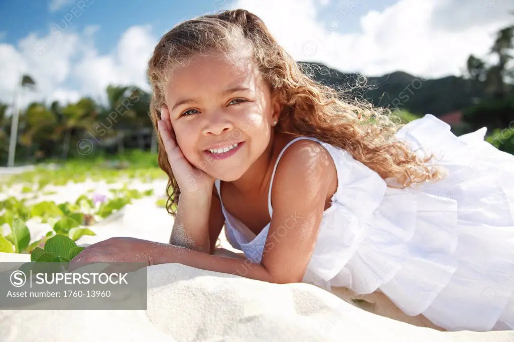 Hawaii, Oahu, Lanikai, Young girl poses laying in sand with hand on her cheek.