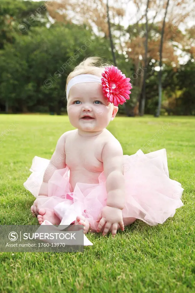 Hawaii, Oahu, Baby girl sits in grass wearing a pink tutu and flower.