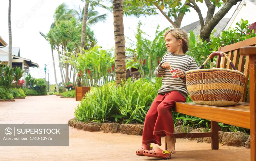 Hawaii, Kauai, Poipu, Kukuiula Shopping Village, Young boy on bench along walkway.