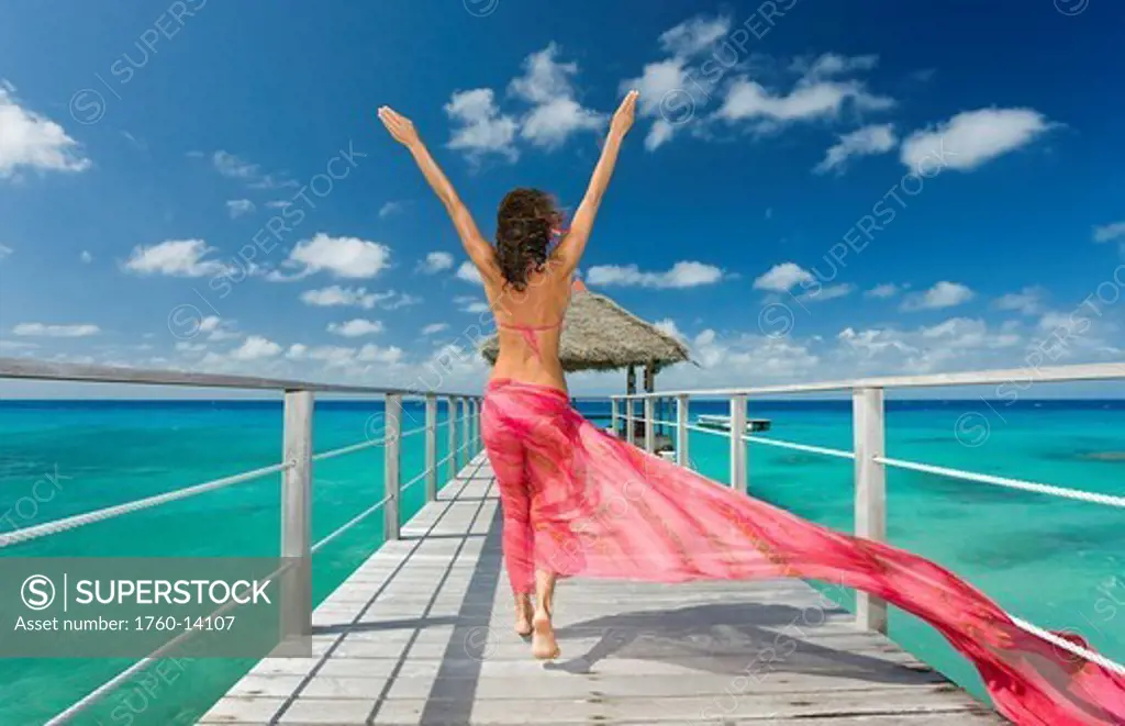 French Polynesia, Tuamotu Islands, Rangiroa Atoll, Woman walking down ocean pier wearing pink pareo, View from behind.