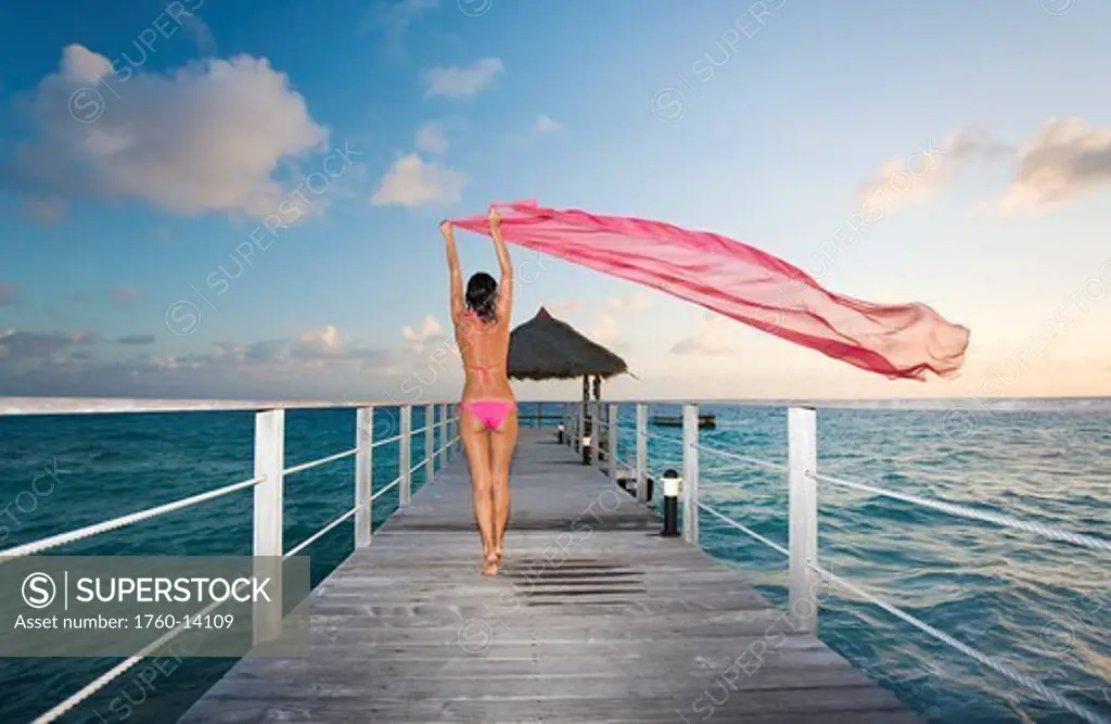 French Polynesia, Tuamotu Islands, Rangiroa Atoll, Woman walking down ocean pier with pink pareo, View from behind.