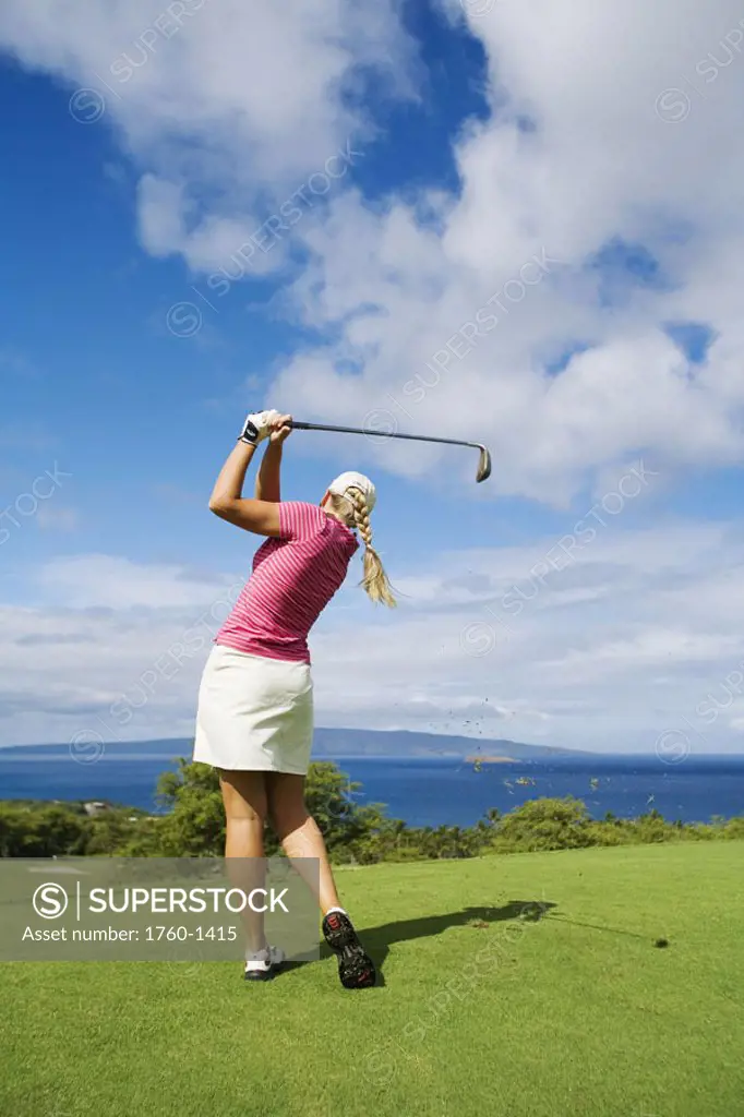 Hawaii, Maui, Wailea Gold Golf Course, Female golfer swinging golf club, view from behind.