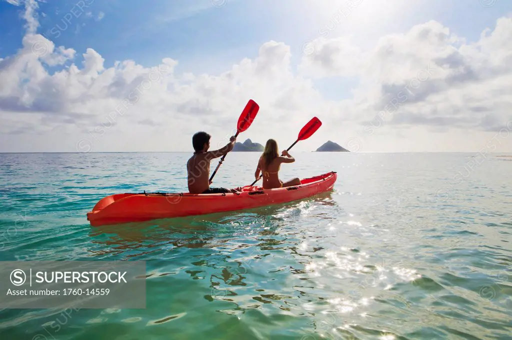 Hawaii, Oahu, Young couple kayaking off Lanikai Beach, Mokulua Islands in distance.