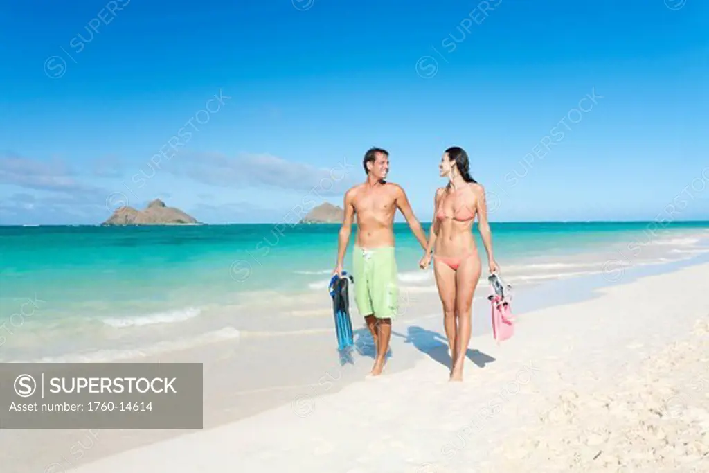 Hawaii, Oahu, Lanikai Beach, Couple walking along seashore with snorkel gear.