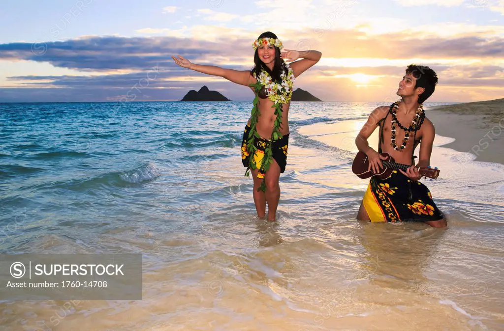 Hawaii, Oahu, Lanikai, Hula dancer couple along beach shoreline at sunrise.