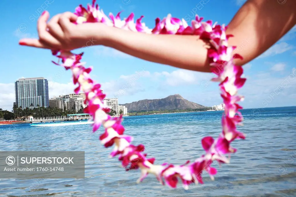 Hawaii, Oahu, Waikiki, Female hand holding an orchid lei framing Diamond Head and Waikiki Beach.