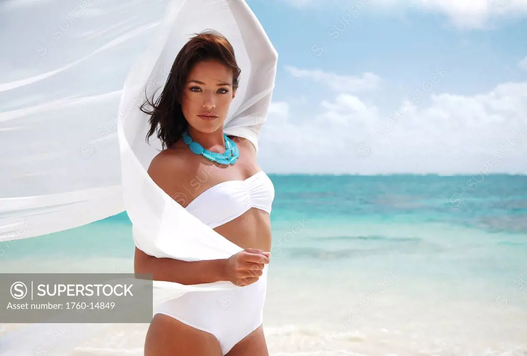 Hawaii, Oahu, Lanikai, Beautiful young woman posing on beach with white fabric blowing in the wind.