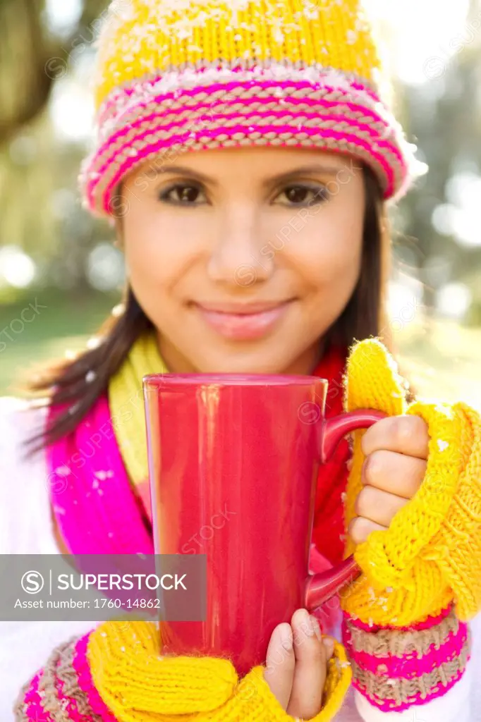 Woman wearing winter clothing in snowy environment, Holding hot drink in mug, Selective focus on mug.
