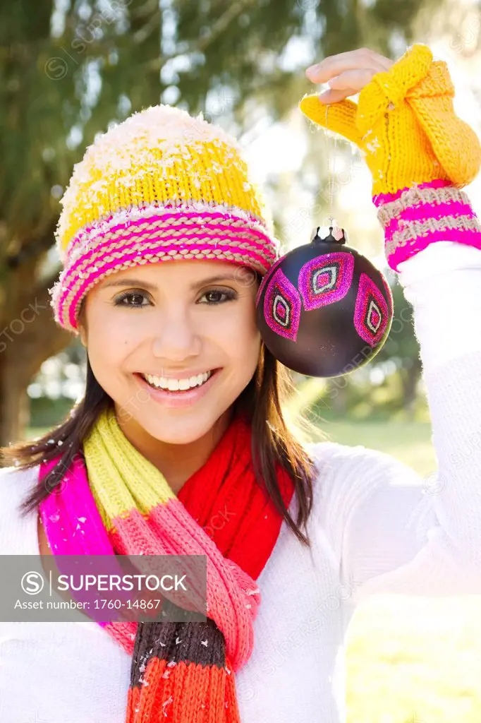 Woman wearing winter clothing in snowy environment, Holding Christmas tree ornament.