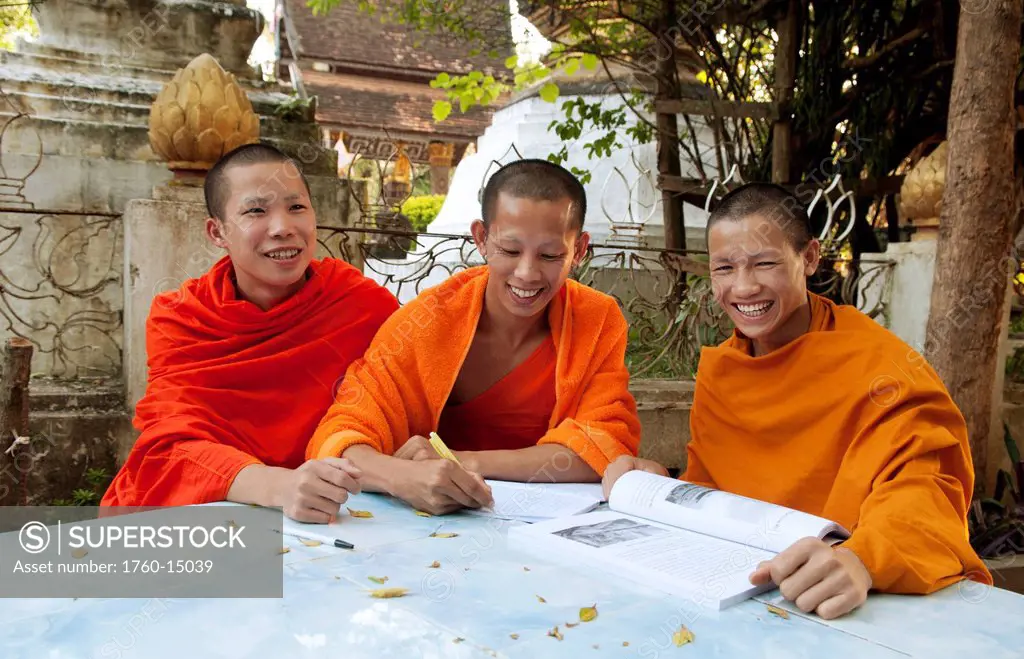 South East Asia, Laos, Luang Prabang, Three young monks sudy in the temple garden.