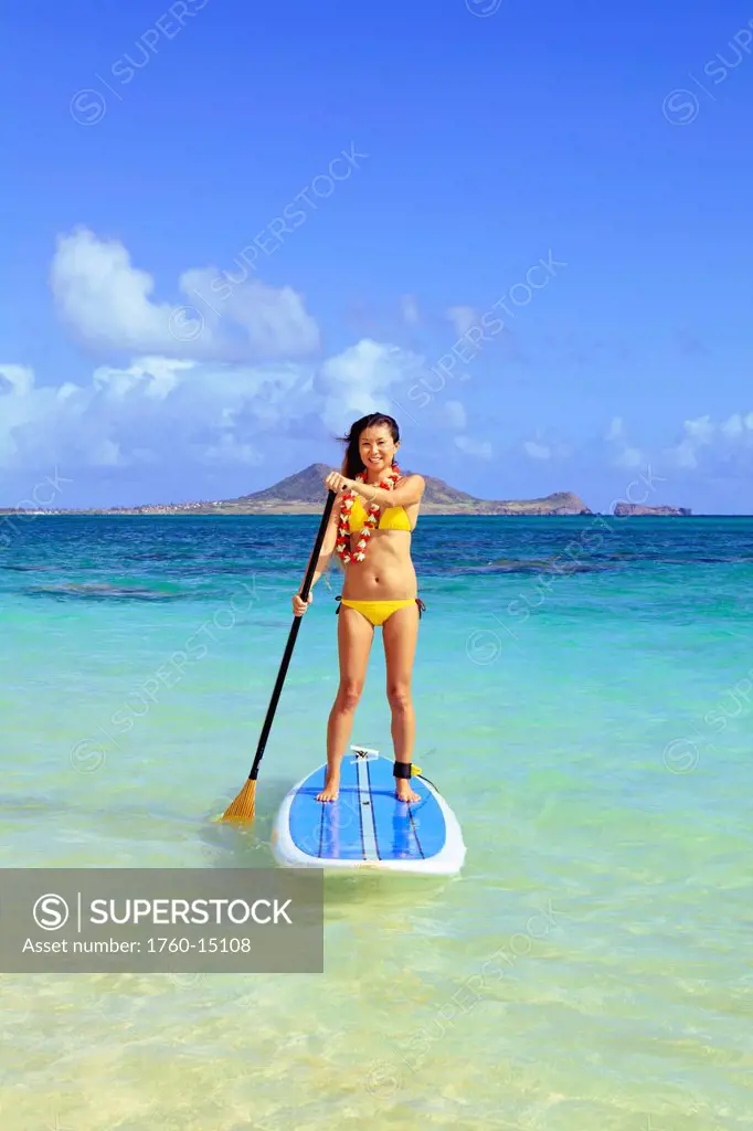 Hawaii, Oahu, Lanikai, Asian women paddle boarding off the beach near Mokulua Island.