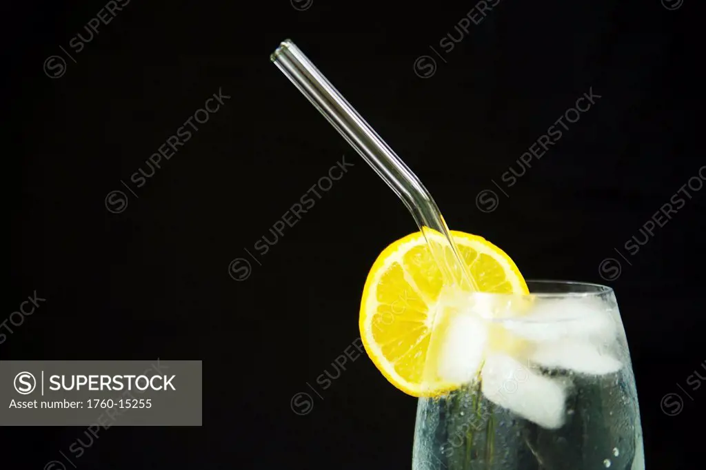 Glass of ice water with lemon and a glass straw.