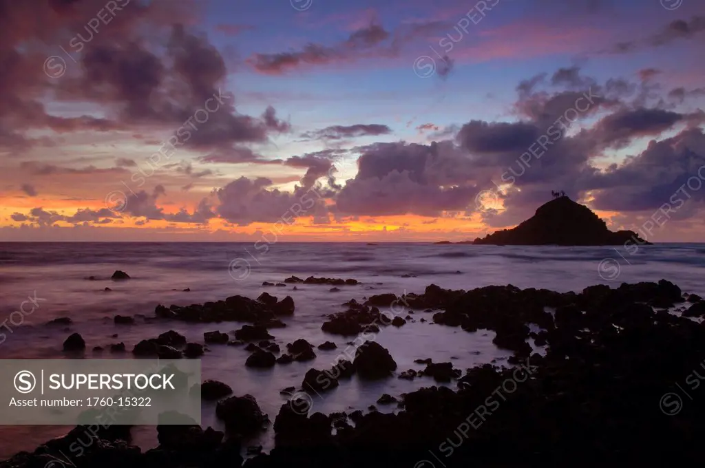 Hawaii, Maui, Hana, Sunrise behind Alau Island viewed from a rocky shoreline.