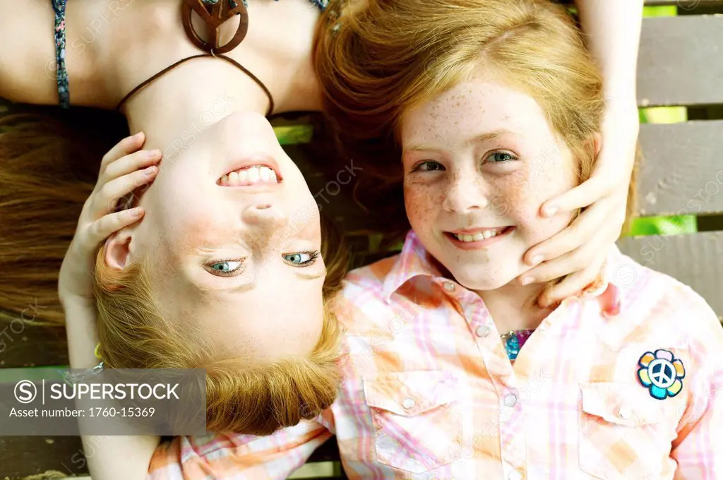 Sisters with freckles and red hair lay facing opposite ways on a porch.