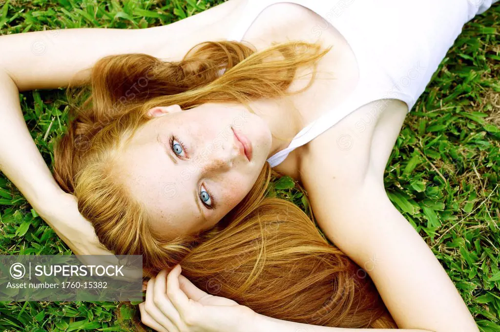Young woman with freckles and red hair lays in the grass and looks up.