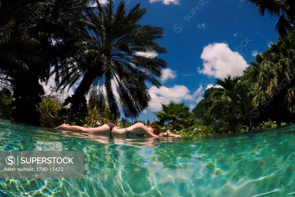 Netherlands Antilles, Caribbean, Curacao, woman lies at the end of an infinity pool with a tropical background.