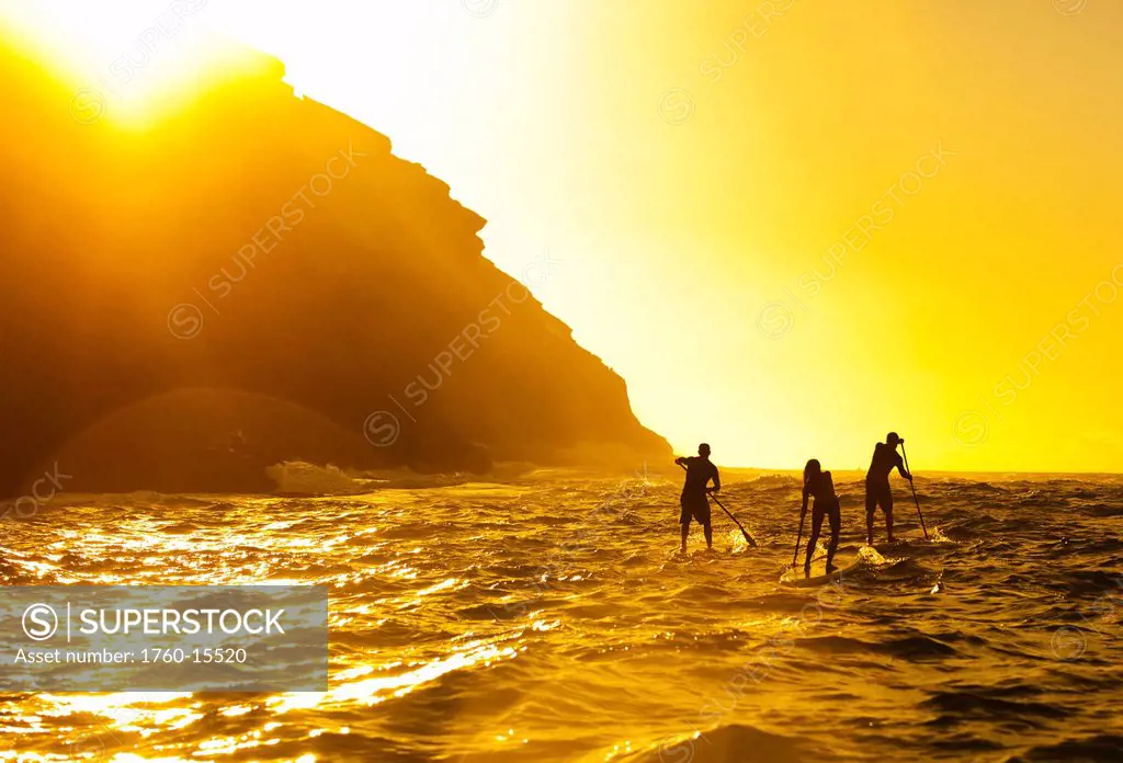 Hawaii, Oahu, Portlock, Three Stand Up Paddlers passing Spitting Caves at sunrise.