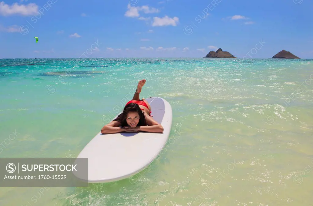 Hawaii, Oahu, Lanikai Beach, Girl floating on surfboard, Mokulua islets in background.