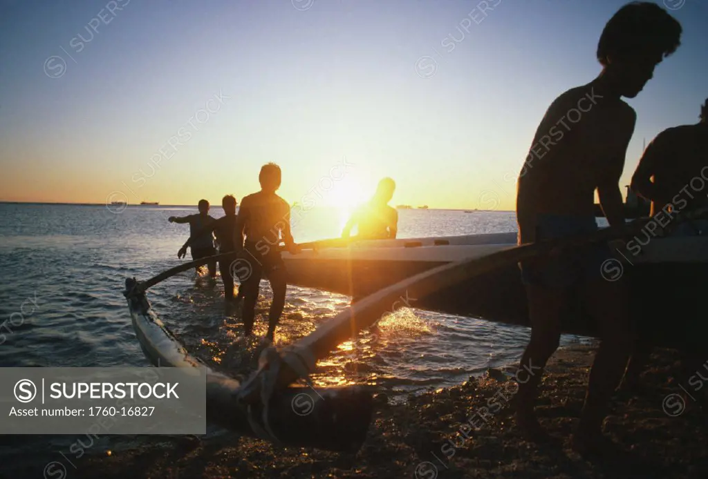 Close-up of paddlers bringing canoe onto beach at sunset, silhouetted by glaring sun.